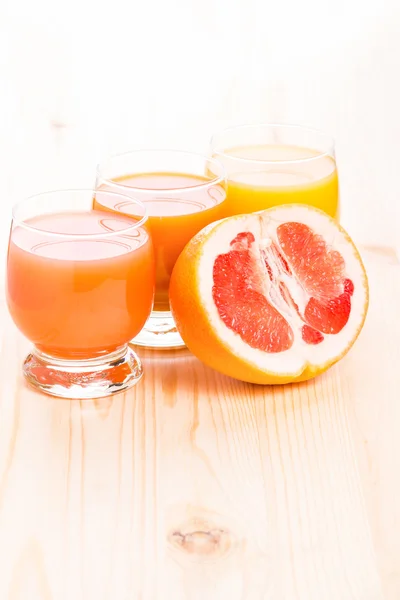 Three glasses of juice with cut in half grapefruit — Stock Photo, Image