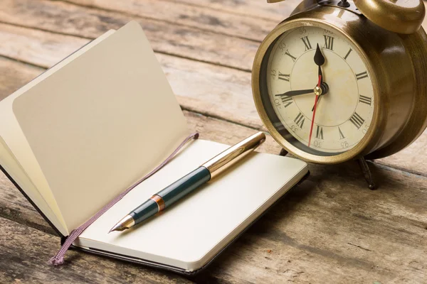 Abra un pequeño portátil con pluma estilográfica y un reloj despertador anticuado detrás — Foto de Stock