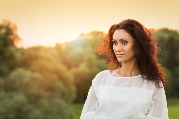 Jeune femme magnifique en robe blanche dans les rayons du coucher de soleil — Photo