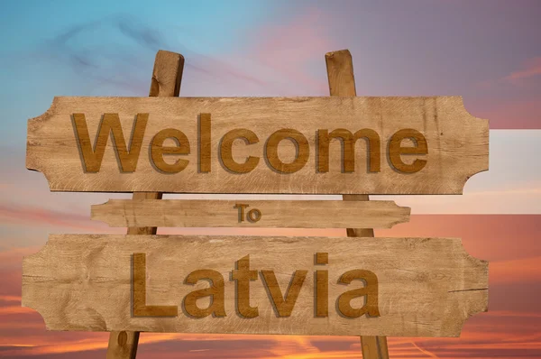 Bienvenido a Letonia signo sobre fondo de madera con la mezcla de la bandera nacional — Foto de Stock