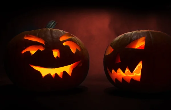 Zwei geschnitzte Gesichter von Kürbissen, die zu Halloween auf rotem Hintergrund leuchten — Stockfoto