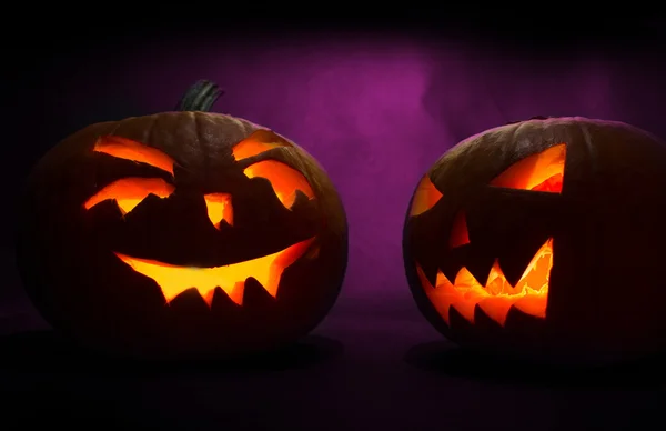 Zwei geschnitzte Gesichter von Kürbissen, die zu Halloween auf violettem Hintergrund leuchten — Stockfoto