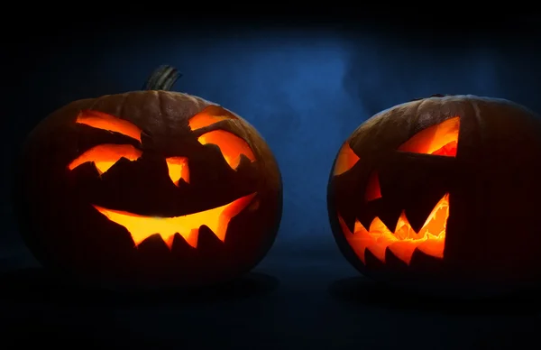 Zwei geschnitzte Gesichter von Kürbissen, die zu Halloween auf blauem Hintergrund leuchten — Stockfoto