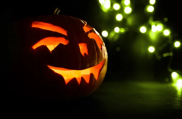 Snidade ansikte av pumpa glödande på Halloween på gröna bokeh ljus bakgrund — Stockfoto