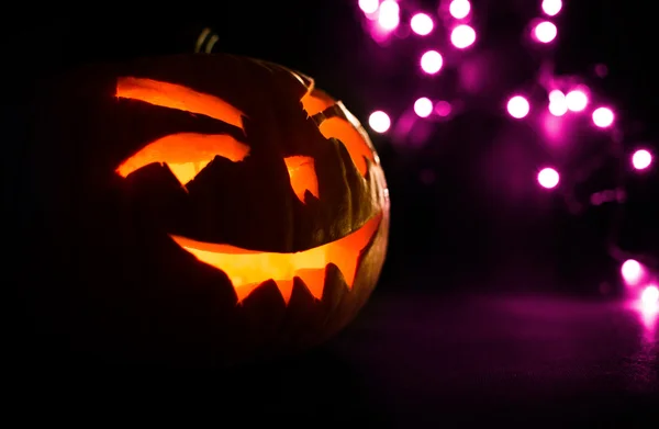 Snidade ansikte av pumpa glödande på Halloween på lila bokeh ljus bakgrund — Stockfoto