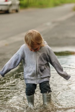 Kız lastik botlarla su birikintisinde oynuyor.