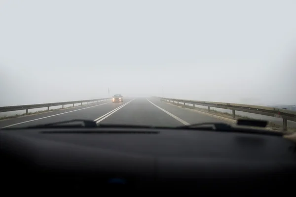 Coche conduciendo en niebla gruesa, visto a través del parabrisas de otro vehículo — Foto de Stock