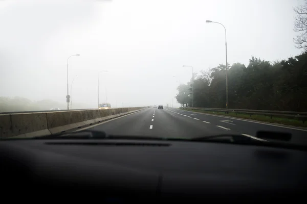 Carro que conduz na névoa grossa, visto através do pára-brisas de outro veículo — Fotografia de Stock