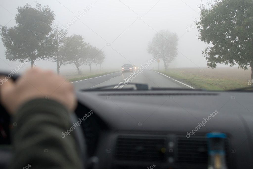 Car driving in thick fog, seen through windscreen of other vehicle