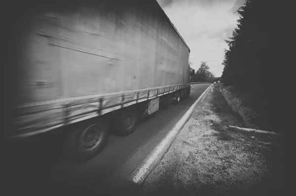 Preto e branco caminhão excesso de velocidade na estrada do país, borrão de movimento — Fotografia de Stock
