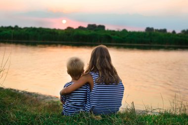 gün batımında, suyun kenarında oturan iki çocuk arkadan görünüm 