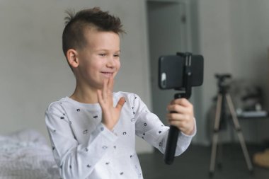Yedi yaşında açık renkli elbiseli bir çocuk, elinde bir telefon tutuyor, fotoğraf çekiyor, arkadaşlarıyla görüntülü konuşma yapıyor, karantinadaki insanlarla iletişim kuruyor. Modern teknolojiler