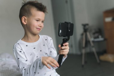 Yedi yaşında açık renkli elbiseli bir çocuk, elinde bir telefon tutuyor, fotoğraf çekiyor, arkadaşlarıyla görüntülü konuşma yapıyor, karantinadaki insanlarla iletişim kuruyor. Modern teknolojiler