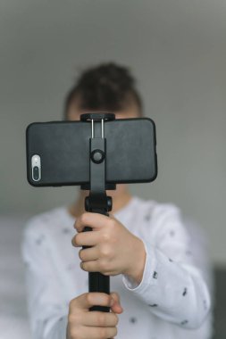 Yedi yaşında açık renkli elbiseli bir çocuk, elinde bir telefon tutuyor, fotoğraf çekiyor, arkadaşlarıyla görüntülü konuşma yapıyor, karantinadaki insanlarla iletişim kuruyor. Modern teknolojiler