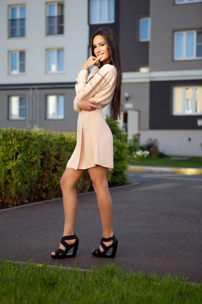 Açık renkli bir yaz elbisesi içinde genç ve güzel bir esmer kadın sıcak bir günde dışarıda poz veriyor.