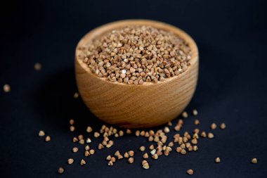 Siyah arka planda, şık bir tahta kupada karabuğday taneleri. Sağlıklı beslenme