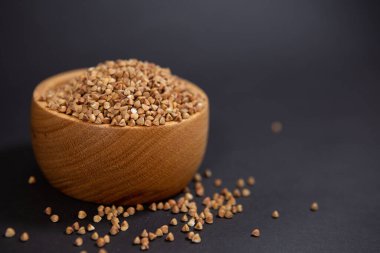 Siyah arka planda, şık bir tahta kupada karabuğday taneleri. Sağlıklı beslenme