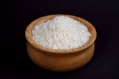 Siyah arka planda izole edilmiş, şık bir ahşap kasede beyaz pirinç taneleri. Yakın plan fotoğraf.