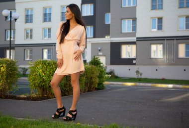 Şehir sokaklarında gülümseyen, yaz aydınlığı elbiseli, çekici, esmer bir kadının resmi.