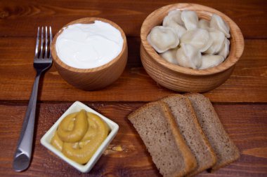 Çavdar ekmeği, ravioli ve hardal ve ekşi kremayla ahşap bir masada hamur köftesi..