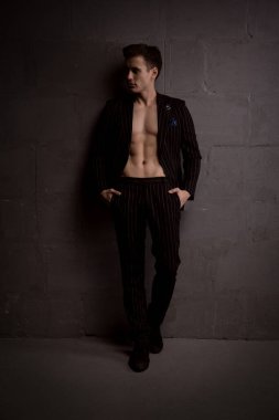 Takım elbiseli kaslı yakışıklı bir adam zayıf bir ışıkta duvara karşı poz veriyor.