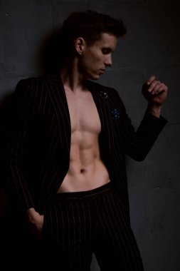 Kaslı vücudu ve düğmesiz ceketi olan yakışıklı, maço bir adam. Koyu arkaplanda moda fotoğrafları