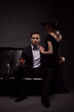 Zarif gece elbiseleri içindeki seksi tutkulu çift loş ışıklı bir odada, karanlık bir kanepede.