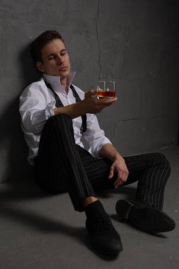 Elinde bir bardak alkolle taş bir duvara yaslanmış düşünceli ve yakışıklı bir gencin portresi..