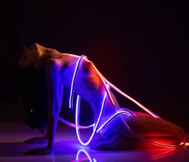 Karanlık bir arka planda neon ışıkta poz veren çıplak, muhteşem bir kadın. Mükemmel kadın vücudu.