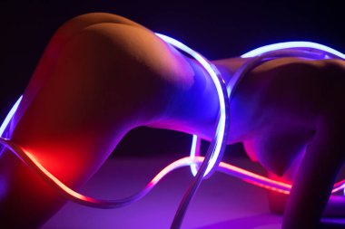 Neon bir kurdelenin ışığında güzel bir vücudu olan muhteşem çıplak bir kadın.