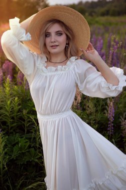 Retro Lady, çiçek açan lupin zeminin güzelliğinden hoşlanıyor. Uyum kavramı. Uzun beyaz bir elbise..