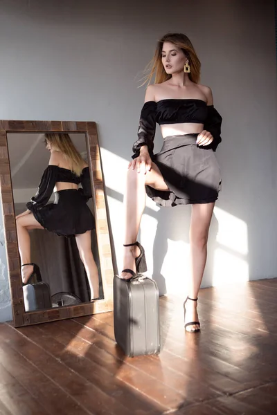 Una hermosa rubia en un vestido negro y un estilo glamoroso posa delante del espejo. —  Fotos de Stock
