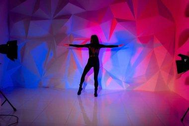 Çok renkli bir duvarın arkasında dans eden bir kadın. Uzun siyah saçlı seksi, zayıf, yalnız kız. Dişi başını tutuyor. parlak renkli geometri arka gruplaması