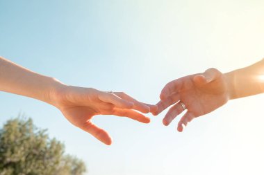 Mavi gökyüzüne karşı alyansları olan iki el birbirine uzanıyor.
