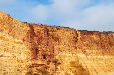 Portekiz 'deki Benagil sahilindeki kayalar. Mavi gökyüzüne karşı kumlu turuncu set tepesi