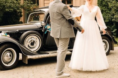 Yeni evliler arabanın yanında sarılıp dans ediyorlar. Gelin ve damat retro arabanın yanında el ele tutuşuyorlar.