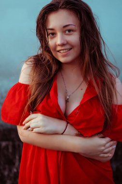 Uzun saçlı, kırmızı elbiseli güzel seksi kız kahkahalar atıyor. Yağmurda çeşmenin yanında dans eden ıslak bir kadın.