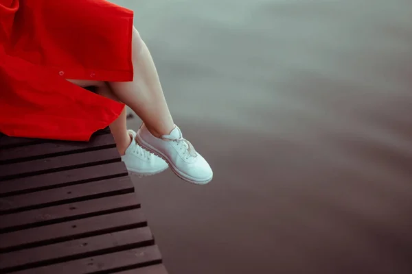 白いトップスを着た赤いドレスを着た美しいセクシーな女の子の足 女性は水のそばに座って チョコレートの眉 — ストック写真