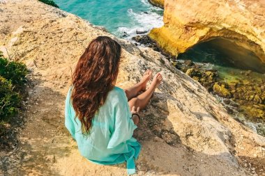 Güzel, seksi bir kız Portekiz 'de bir kayanın üzerinde oturuyor. Okyanusun arka görüntüsü