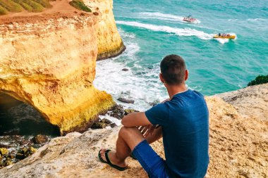Portekiz 'de taş üstünde gözlüklü, ince, yakışıklı bir adam oturuyor. Okyanusun arka görüntüsü