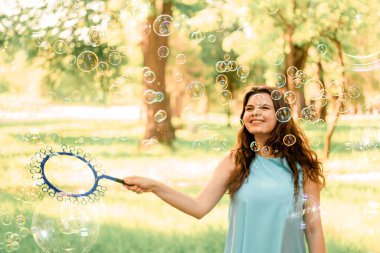Güzel neşeli kız parkta durur ve sabun köpüklerini şişirir.