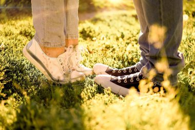 Bir erkek ve bir kız yeşil çimlerin üzerinde karşı karşıya duruyorlar, ayakları spor ayakkabılarla bağlanmış, bir yaz buluşması, yatay görüntüler.