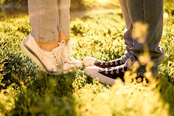 a guy and a girl stand opposite each other on the green grass, their feet are shod in sneakers, a summer meeting, horizontal imag