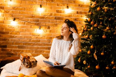 Siyah saçlı beyaz kazaklı güzel kıvırcık kız yatağa oturup gülümsüyor ve bir deftere yazıyor. Mutlu yıllar portresi, bir dilek tutar ve bir mektup yazar.