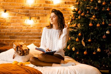 Siyah saçlı beyaz kazaklı güzel kıvırcık kız yatağa oturup gülümsüyor ve bir deftere yazıyor. Mutlu yıllar portresi, bir dilek tutar ve bir mektup yazar.