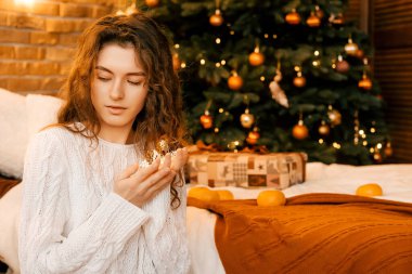 Siyah saçlı, beyaz kazaklı güzel kıvırcık kız ellerinde bir yıldız çelengi tutuyor. Yeni yıl portresi