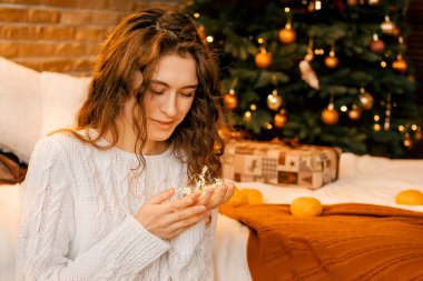 Siyah saçlı, beyaz kazaklı güzel kıvırcık kız ellerinde bir yıldız çelengi tutuyor. Yeni yıl portresi