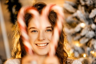 Kıvırcık saçlı güzel bir kız ağacın yanında duruyor, yeni yıl fotoğrafında şeker lolipopu var.