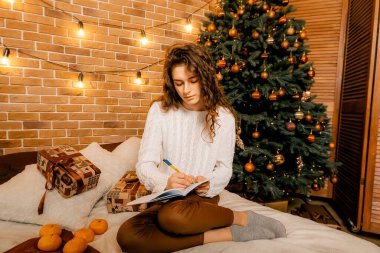 Siyah saçlı beyaz kazaklı güzel kıvırcık kız yatağa oturup gülümsüyor ve bir deftere yazıyor. Mutlu yıllar portresi, bir dilek tutar ve bir mektup yazar.