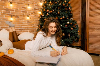 Siyah saçlı beyaz kazaklı güzel kıvırcık kız yatağa uzanıp gülümsüyor ve bir deftere yazıyor. Mutlu yıllar portresi, bir dilek tutar ve bir mektup yazar.